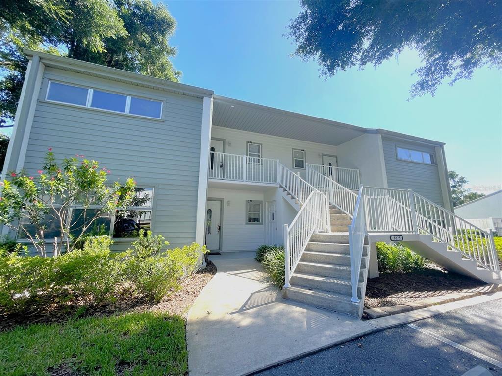 A two-story apartment building exterior features light gray siding, white railings, and an outdoor staircase — 6825 E DOWNING STREET UNIT 433, INVERNESS, FL