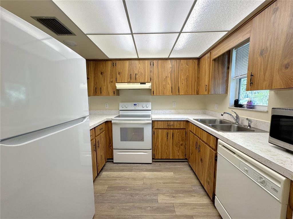 A kitchen features wood cabinets, white appliances, laminate countertops, and a drop ceiling — 6825 E DOWNING STREET UNIT 433, INVERNESS, FL