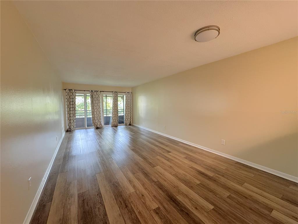 An empty living room features light wood-look flooring, beige walls, and sliding glass balcony doors — 6825 E DOWNING STREET UNIT 433, INVERNESS, FL