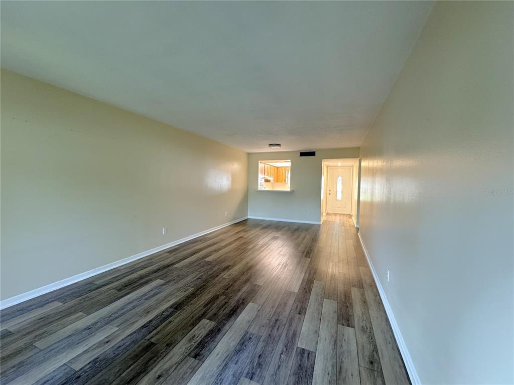 An empty living room features light-colored walls, wood-look flooring, and a pass-through to the kitchen — 6825 E DOWNING STREET UNIT 433, INVERNESS, FL