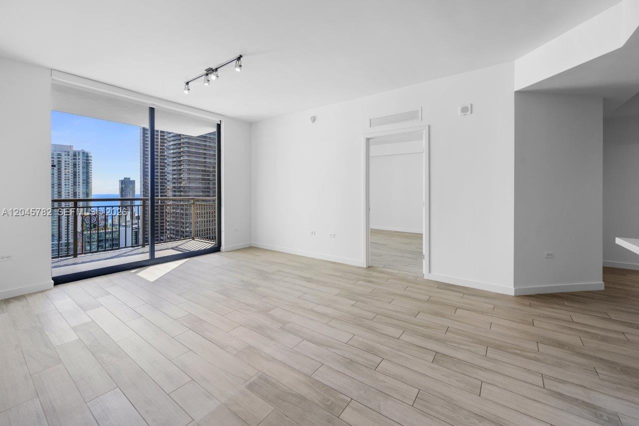 An empty living room features light wood-look tile flooring, white walls, and a balcony view — 999 SW 1st Ave # 2911, Miami FL 33130, MIAMI, FL