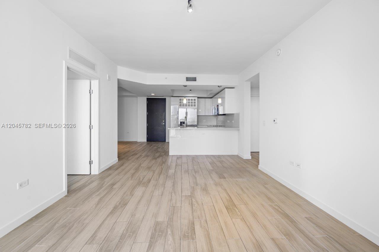 An open-concept living area features light wood-look flooring and a kitchen with white cabinetry — 999 SW 1st Ave # 2911, Miami FL 33130, MIAMI, FL
