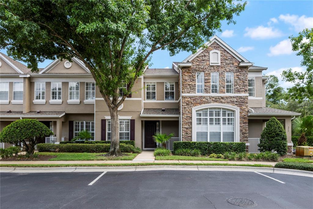 A two-story townhouse with a stone facade, tan siding, and a large front tree — 573 SHINING ARMOR LANE, LONGWOOD, FL