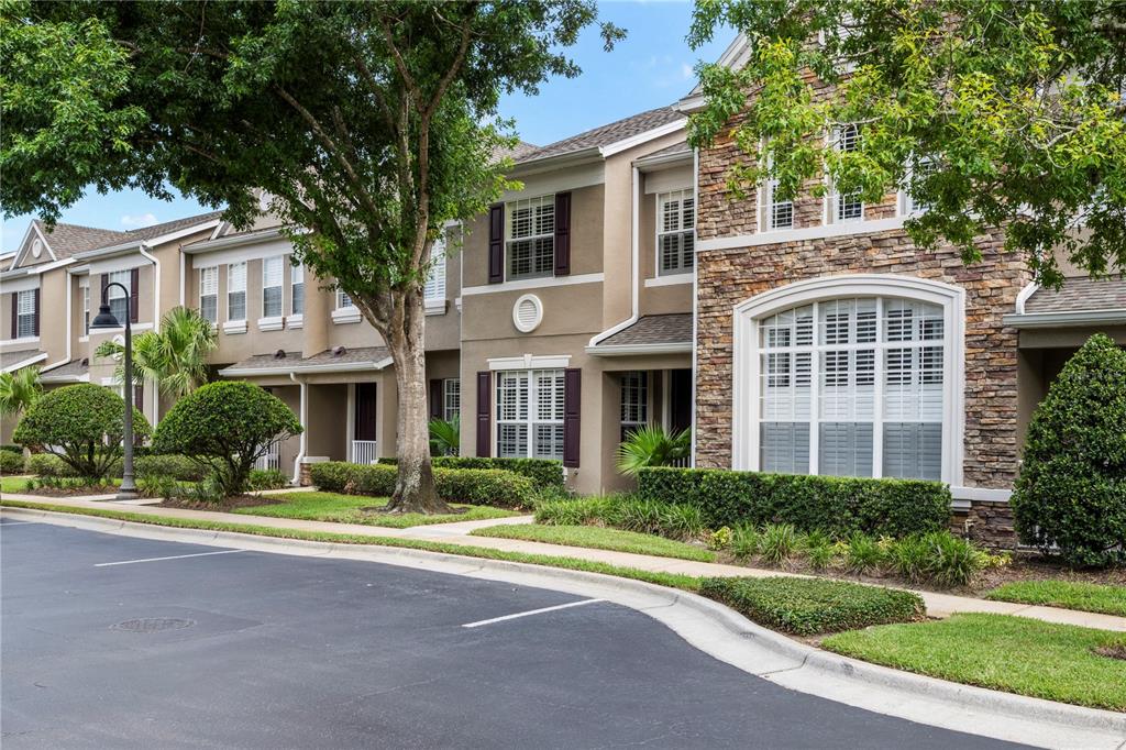 A multi-story townhouse complex with stone and stucco siding, landscaping, and a paved parking area — 573 SHINING ARMOR LANE, LONGWOOD, FL