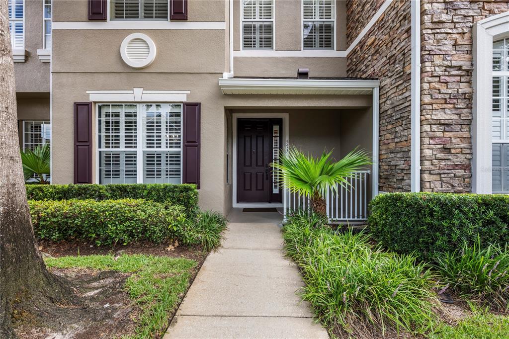 A concrete walkway leads to the front entrance of a two-story townhouse with stone siding — 573 SHINING ARMOR LANE, LONGWOOD, FL