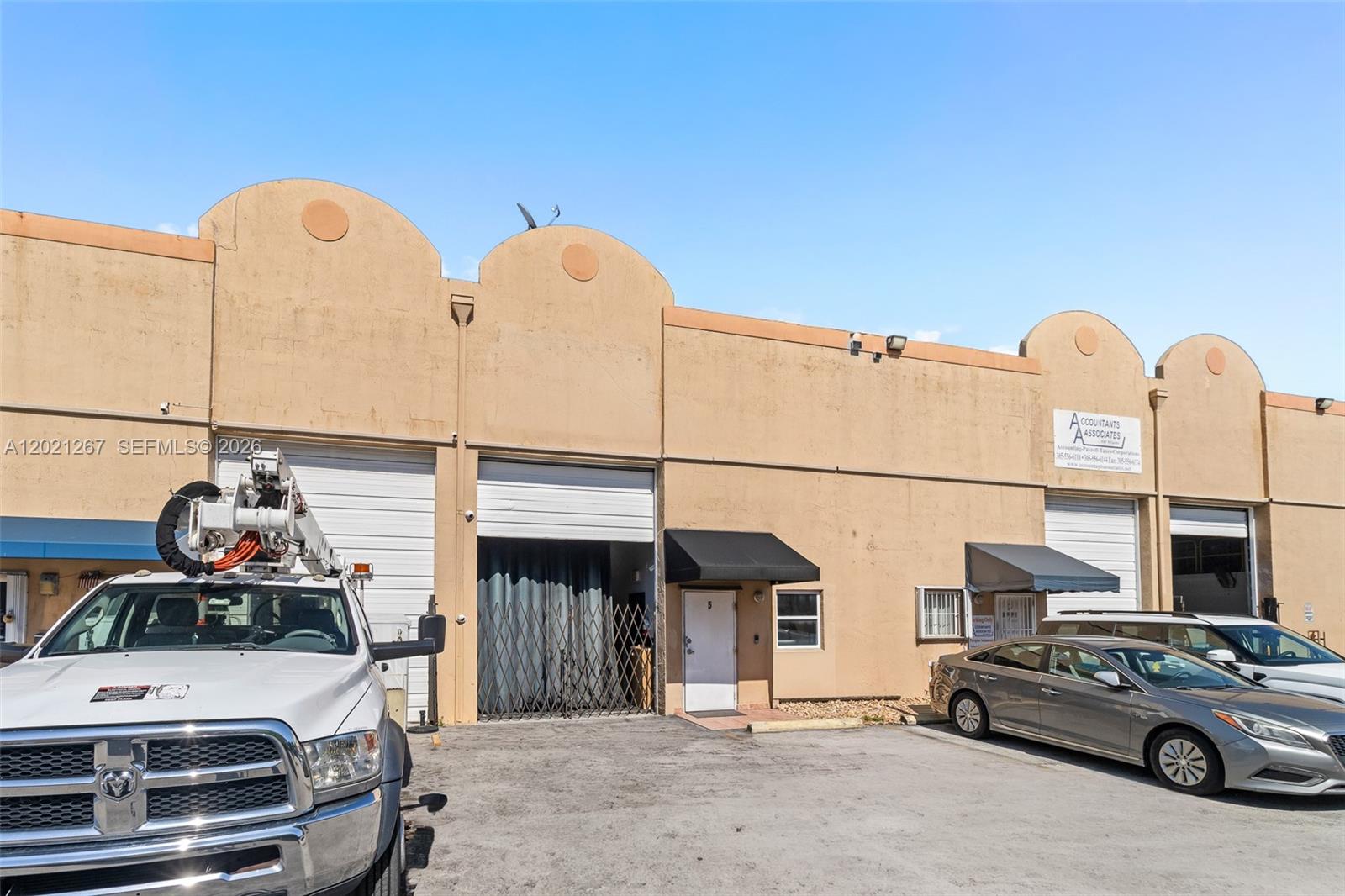 A beige commercial building features multiple roll-up garage doors and a parking lot in front — 1745 W 37th St # 5, Hialeah FL 33012, HIALEAH, FL