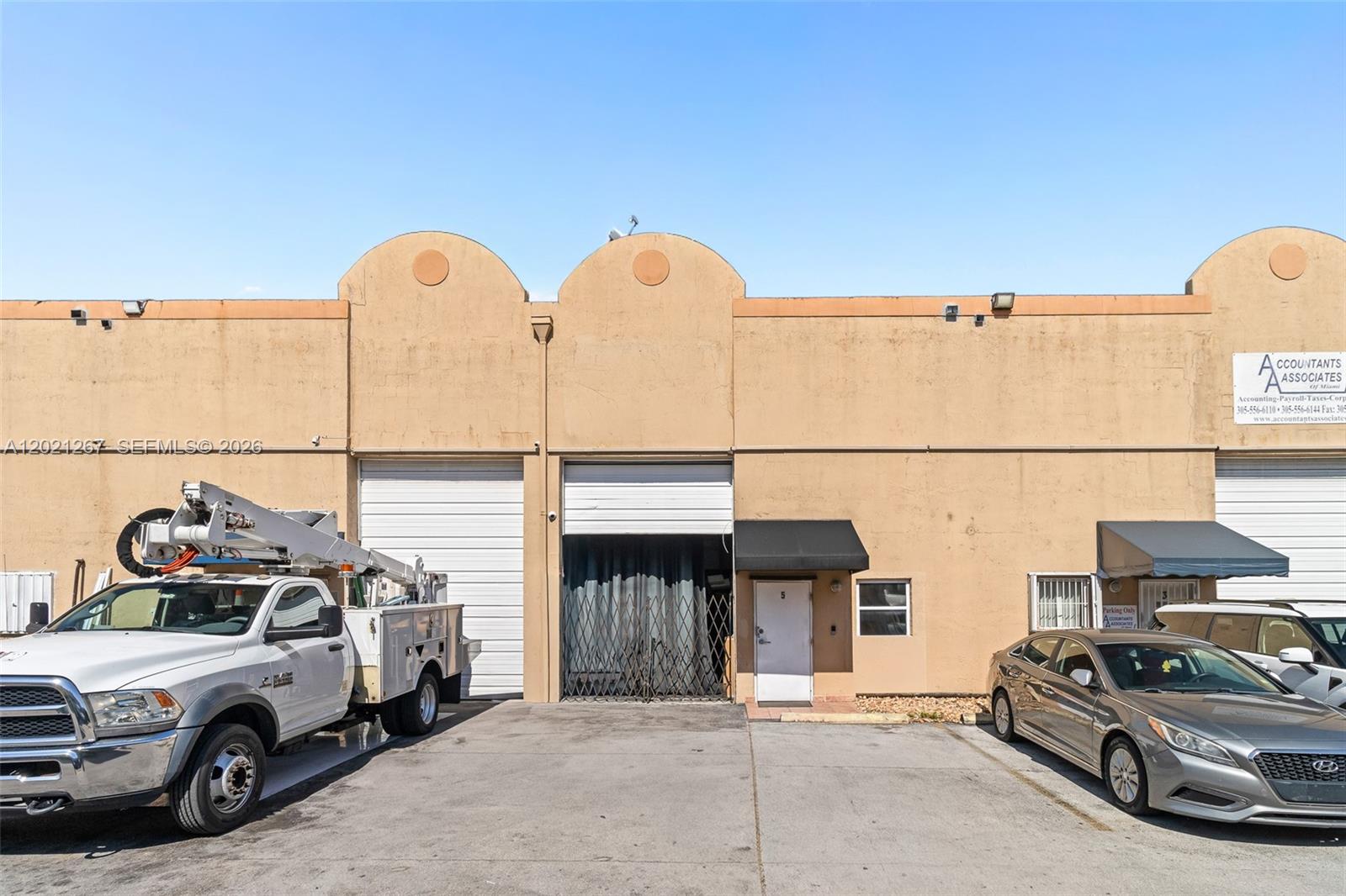 An exterior view of a commercial building with two roll-up doors and two parked vehicles — 1745 W 37th St # 5, Hialeah FL 33012, HIALEAH, FL