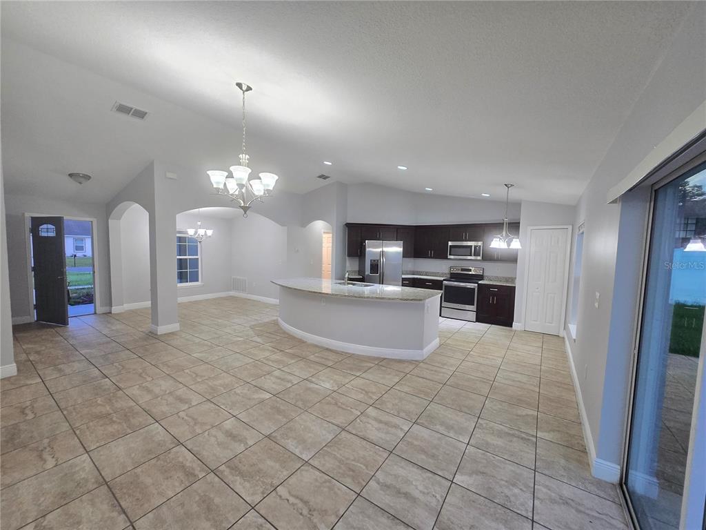 An open-concept kitchen and dining area features tile flooring, dark cabinets, and a curved island — 356 GARDENIA COURT, POINCIANA, FL