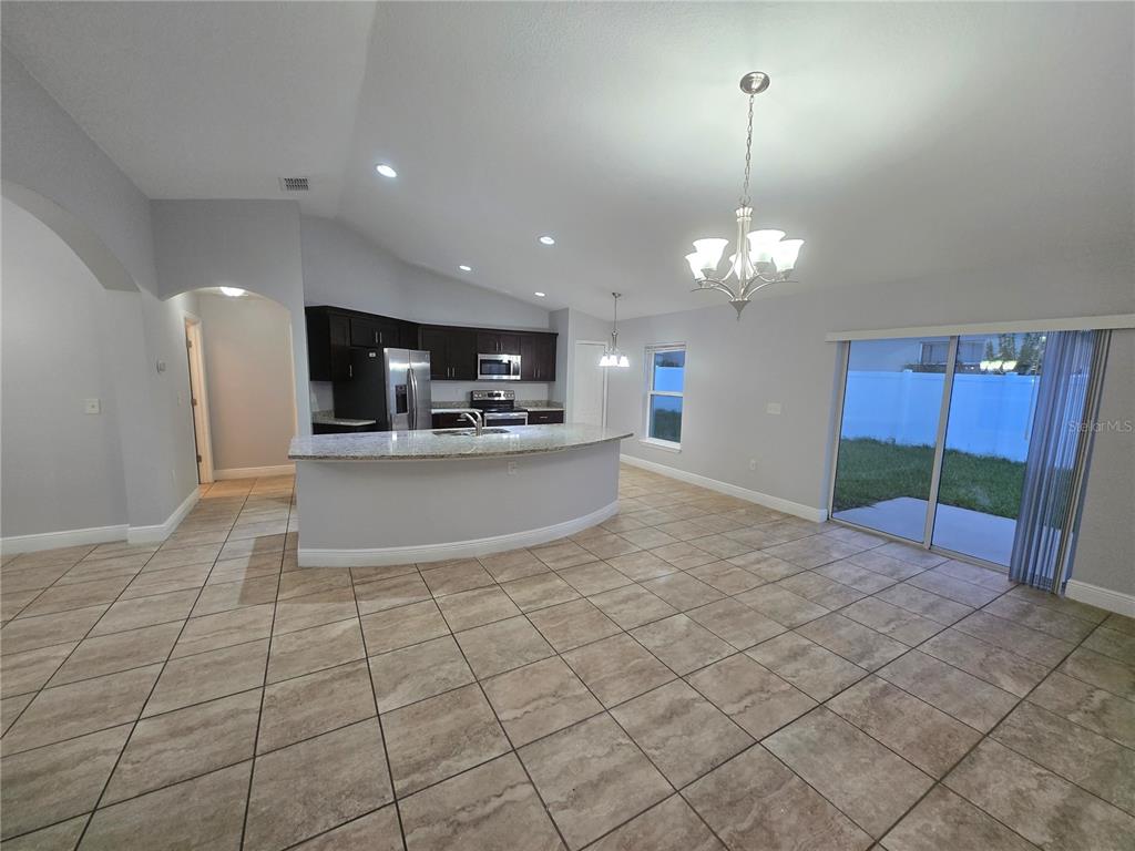 A kitchen with dark cabinets and a curved granite island opens to a tiled dining area — 356 GARDENIA COURT, POINCIANA, FL