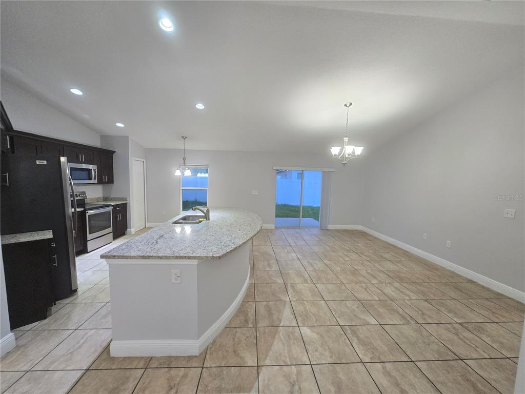 An open-concept kitchen and dining area features dark cabinets, granite countertops, and tile flooring — 356 GARDENIA COURT, POINCIANA, FL