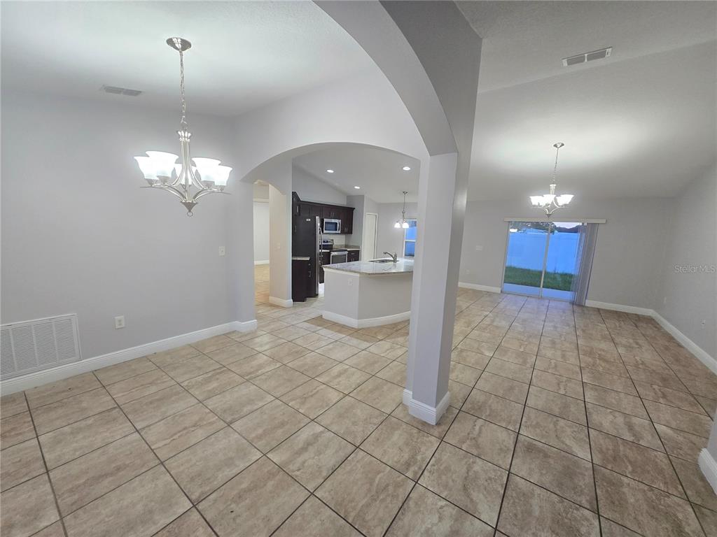 An open-concept dining area and kitchen feature tile flooring, arched entryways, and two chandeliers — 356 GARDENIA COURT, POINCIANA, FL