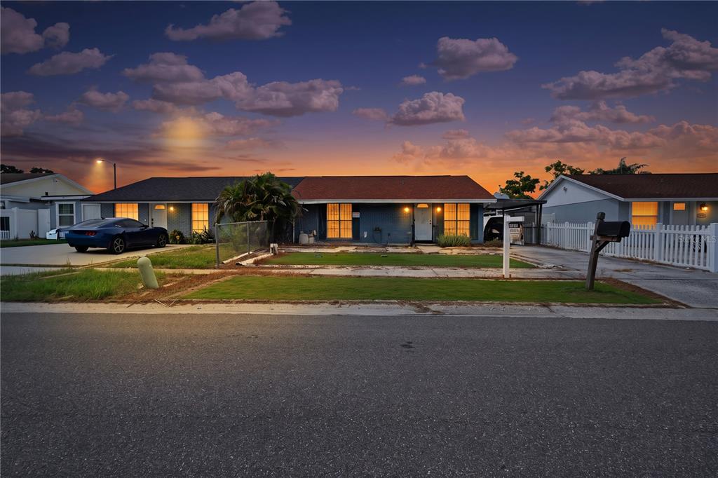 A single-story duplex with a brick facade, two driveways, and a sunset sky background — 8584 BRIAR GROVE CIRCLE, TAMPA, FL
