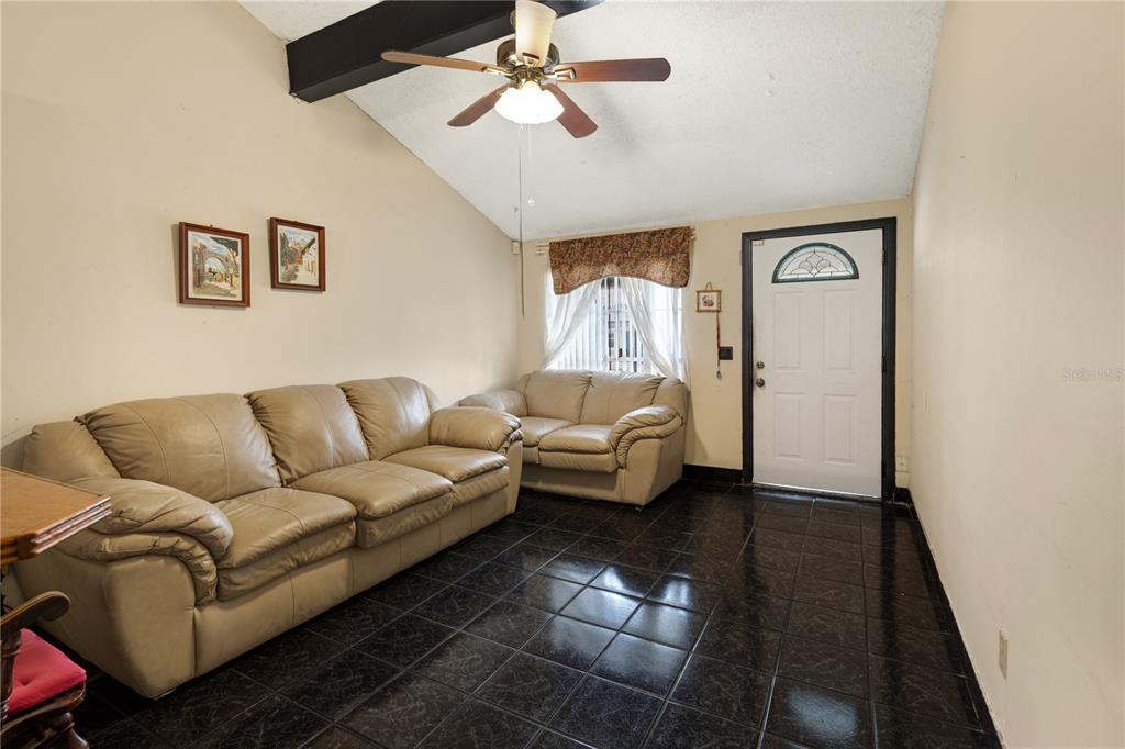 A living room features beige leather sofas, dark tiled floors, and a vaulted ceiling with a fan — 8584 BRIAR GROVE CIRCLE, TAMPA, FL