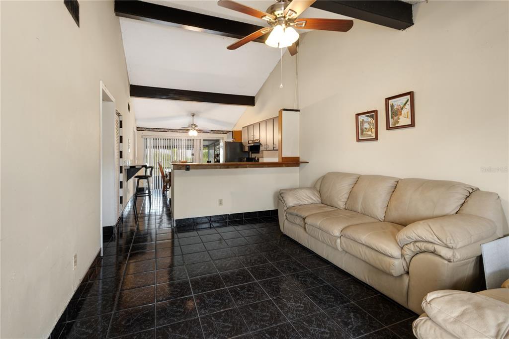 A living room with dark tile floors, a beige sofa, and a vaulted ceiling with beams — 8584 BRIAR GROVE CIRCLE, TAMPA, FL