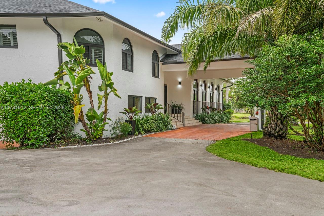 A white two-story house features a covered driveway entrance, arched windows, and lush landscaping — 14875 SW 212th St, Miami FL 33187, MIAMI, FL
