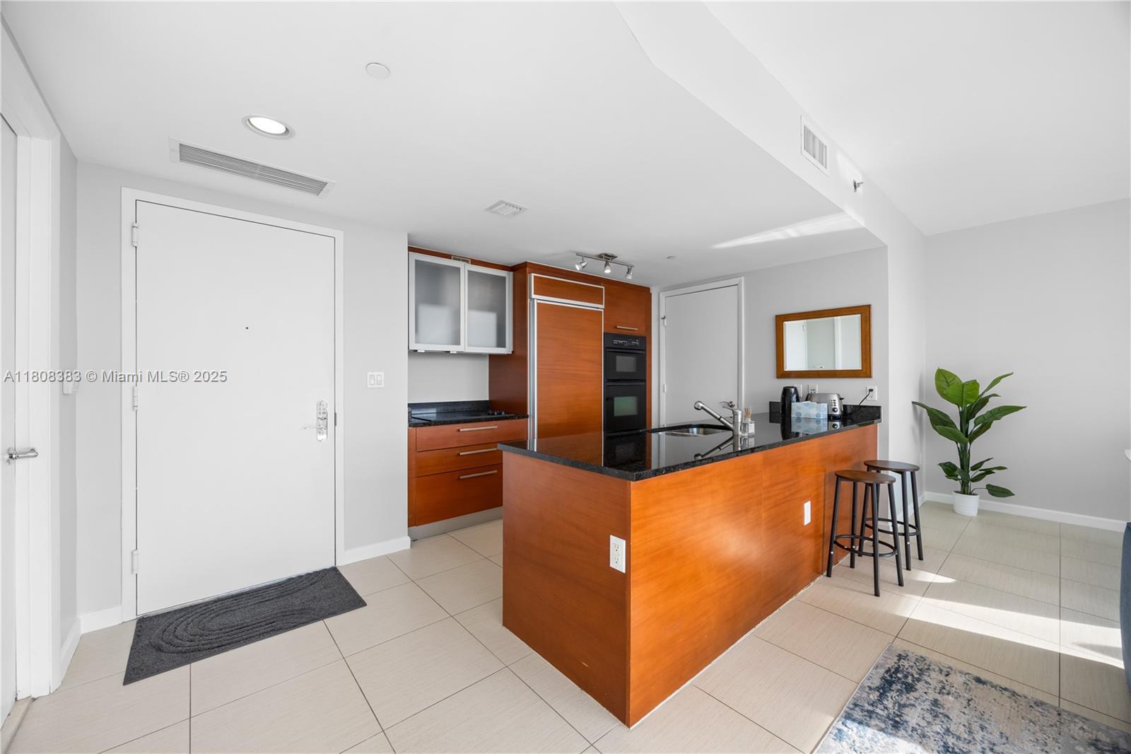 A kitchen features wood cabinetry, a black granite island, and two bar stools — 1830 S Ocean Dr # 1807, Hallandale Beach FL 33009, HALLANDALE BEACH, FL