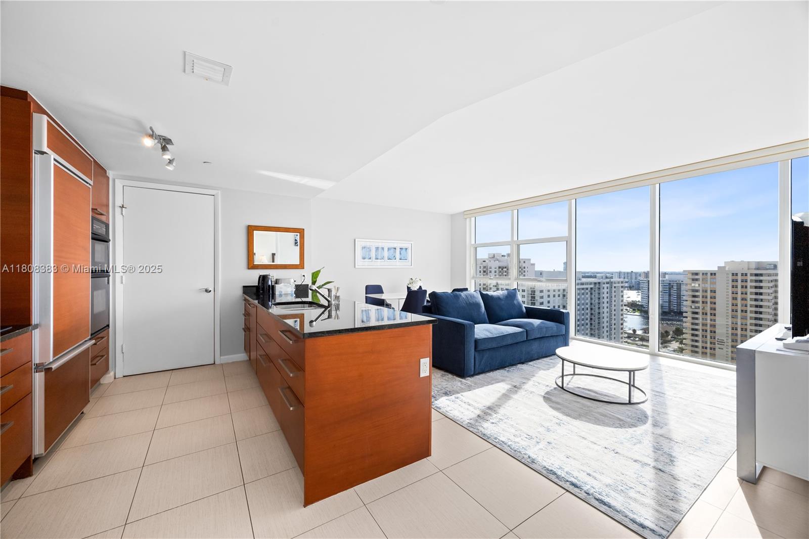 A modern kitchen with wood cabinets and a living area featuring floor-to-ceiling windows — 1830 S Ocean Dr # 1807, Hallandale Beach FL 33009, HALLANDALE BEACH, FL
