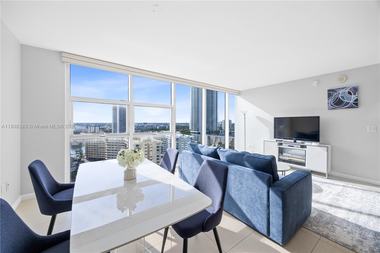 A bright living and dining area features blue furniture, a white table, and floor-to-ceiling windows — 1830 S Ocean Dr # 1807, Hallandale Beach FL 33009, HALLANDALE BEACH, FL