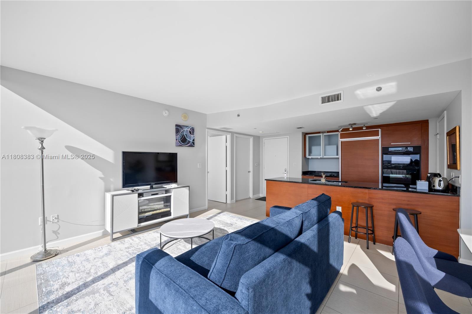 A living room features a blue sofa, a television console, and an open-concept kitchen area — 1830 S Ocean Dr # 1807, Hallandale Beach FL 33009, HALLANDALE BEACH, FL