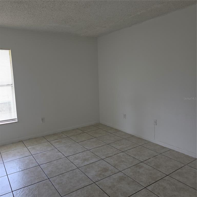 An empty room features white walls, a textured ceiling, and light-colored square floor tiles — 921 W OAK RIDGE ROAD UNIT 921C, ORLANDO, FL