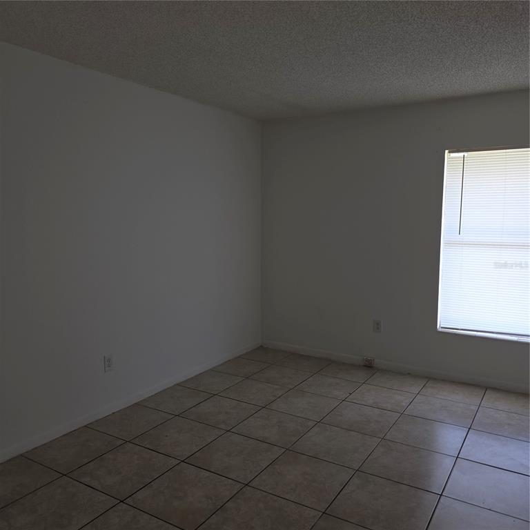 An empty room features white walls, a window with blinds, and light-colored tile flooring — 921 W OAK RIDGE ROAD UNIT 921C, ORLANDO, FL