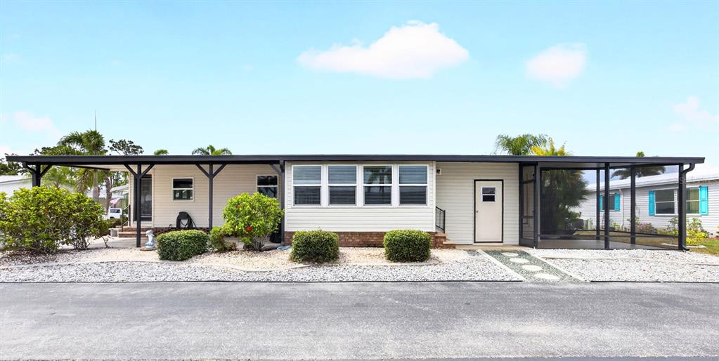 A single-story manufactured home features a long covered porch, a carport, and landscaped bushes — 15550 BURNT STORE ROAD UNIT 164, PUNTA GORDA, FL