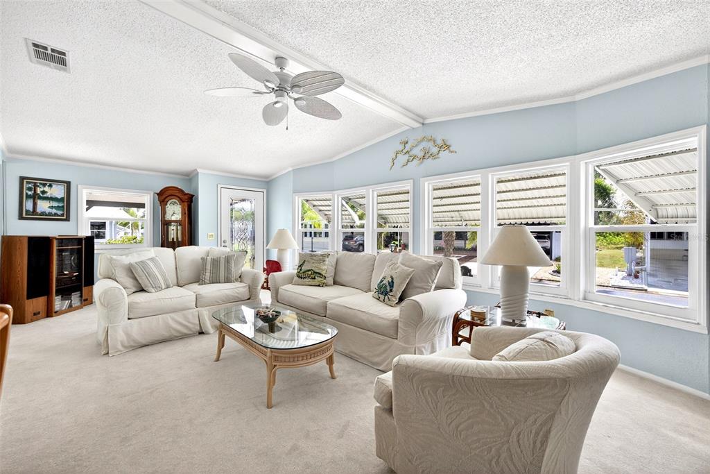 A living room features light blue walls, white furniture, a ceiling fan, and large windows — 15550 BURNT STORE ROAD UNIT 164, PUNTA GORDA, FL