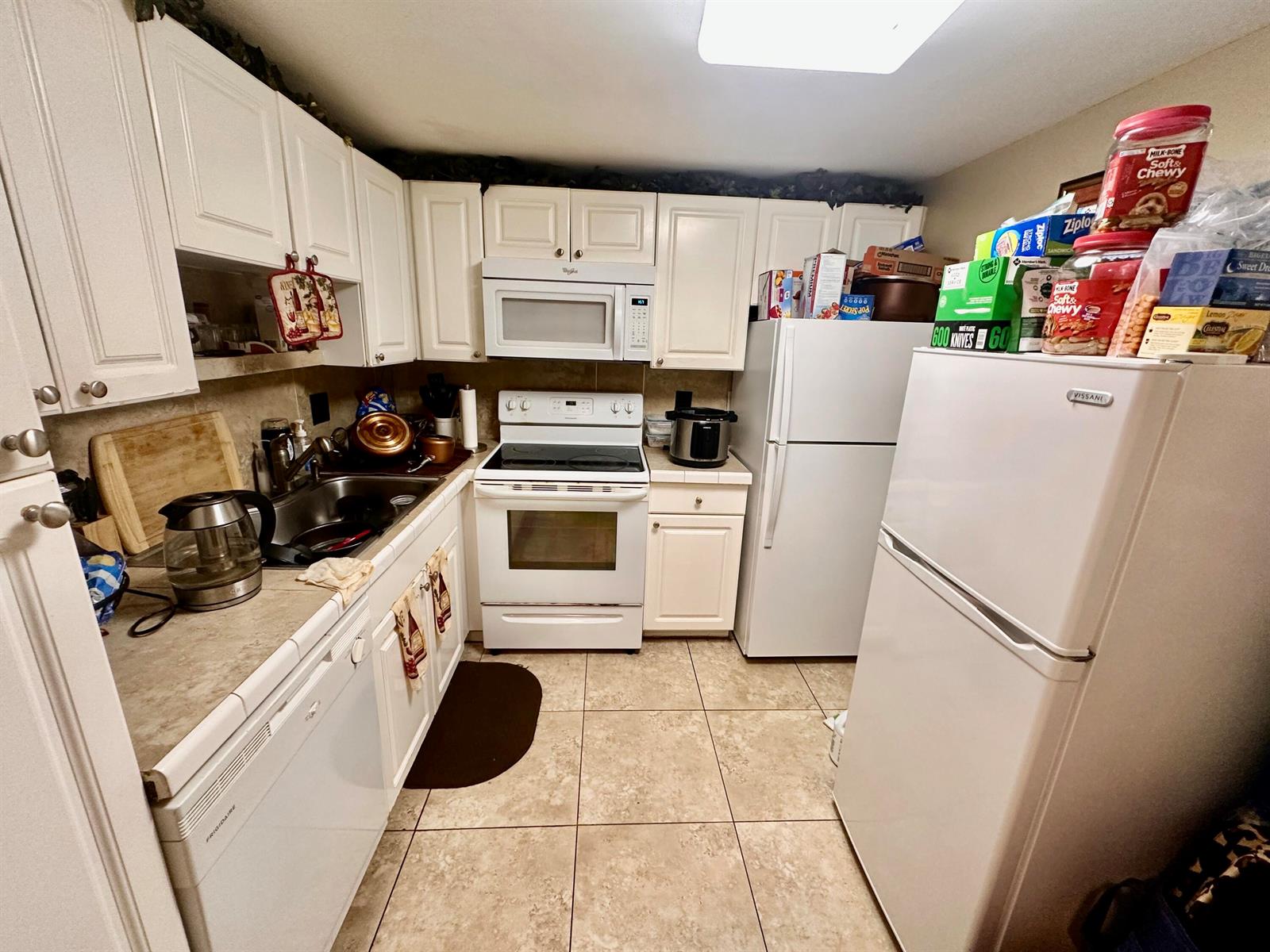 A kitchen features white cabinets, white appliances, tile flooring, and a double refrigerator setup — 1505 CRESCENT Circle # A12, Lake Park FL 33403, LAKE PARK, FL