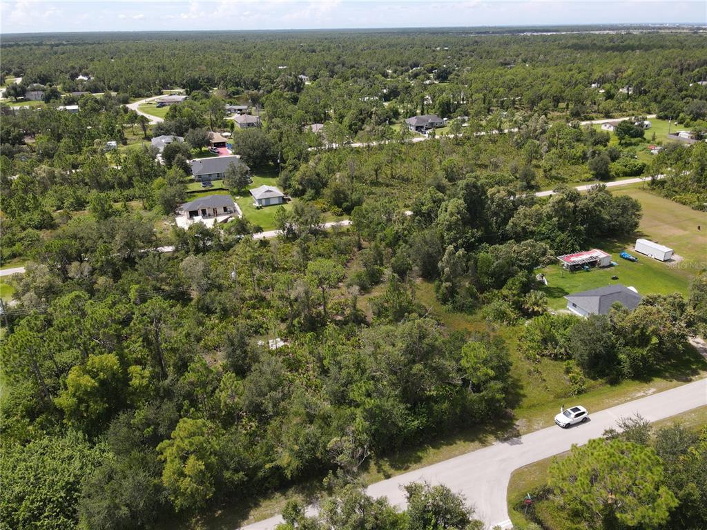 An aerial view shows a wooded residential lot with a nearby road and several houses — 27487 SENATOR DRIVE, PUNTA GORDA, FL