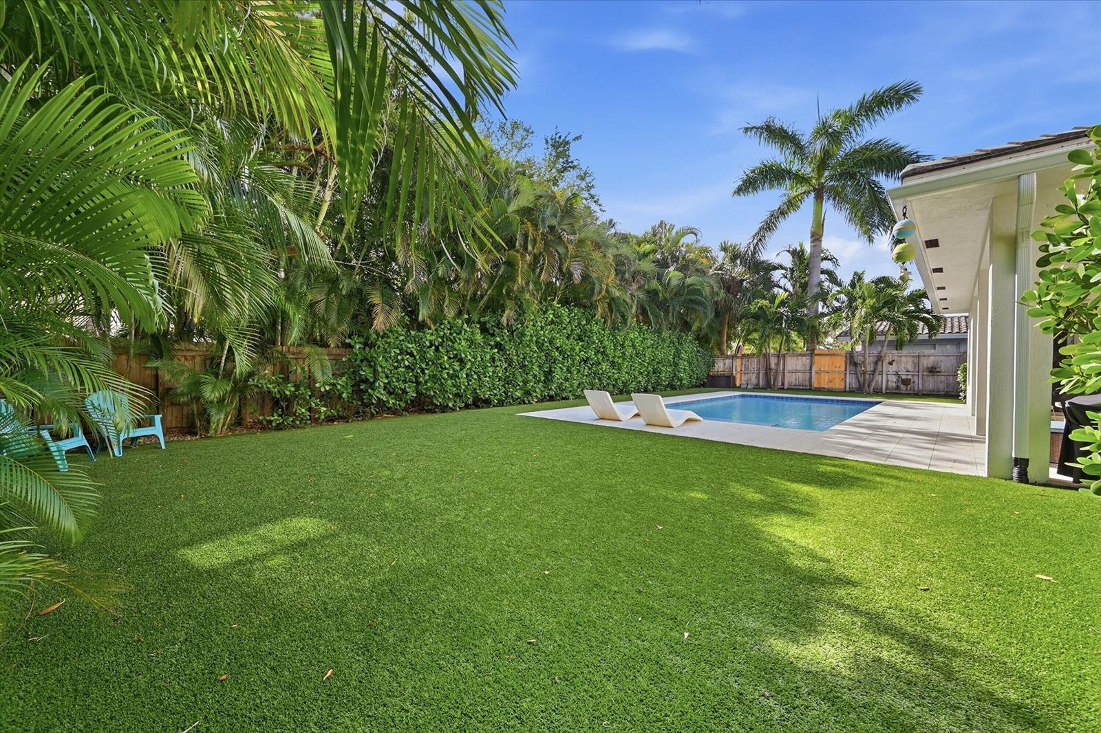 A backyard features a swimming pool, lounge chairs, artificial turf, and lush tropical landscaping — 2840 NE 22nd Avenue, Lighthouse Point FL 33064, LIGHTHOUSE POINT, FL