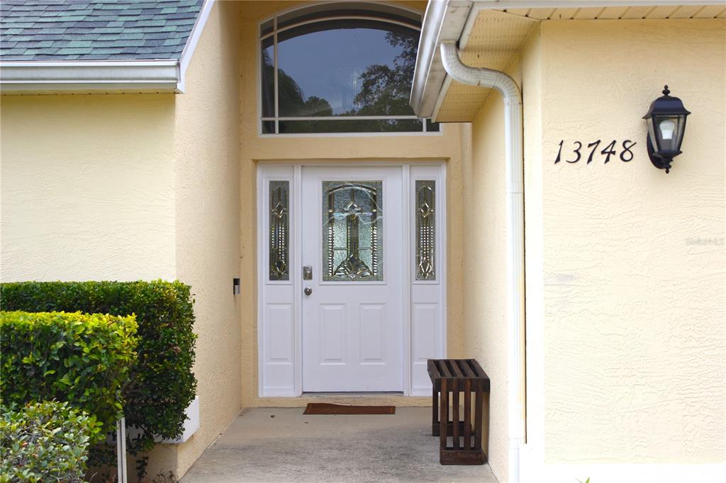 A white front door with decorative glass panels is set in a light yellow exterior wall — 13748 MEADE COURT, HUDSON, FL
