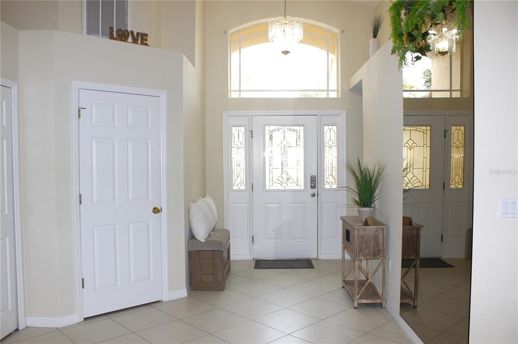 A bright foyer features tile flooring, a high ceiling, a front door with sidelights, and mirrors — 13748 MEADE COURT, HUDSON, FL