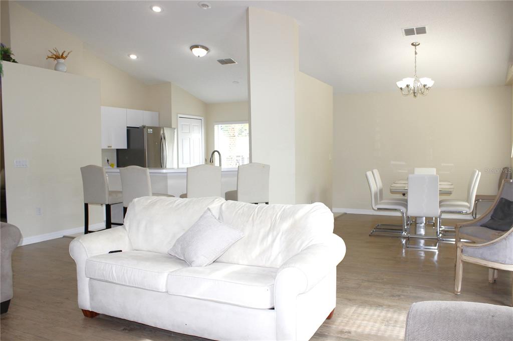 An open-concept living and dining area features a white sofa, breakfast bar, and dining table — 13748 MEADE COURT, HUDSON, FL