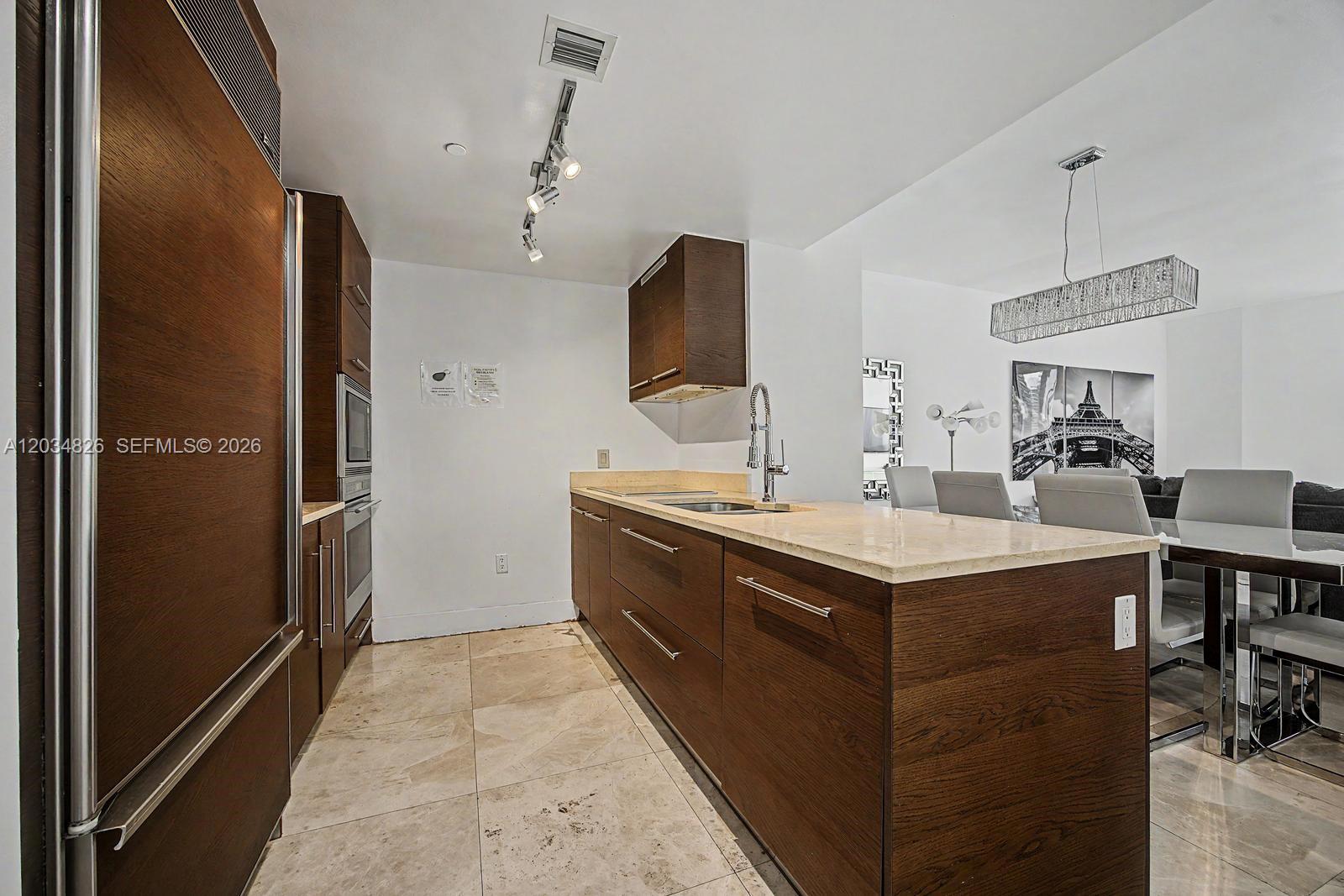 A modern kitchen features dark wood cabinetry, beige stone countertops, and light tile flooring — 485 Brickell Ave # 2209, Miami FL 33131, MIAMI, FL