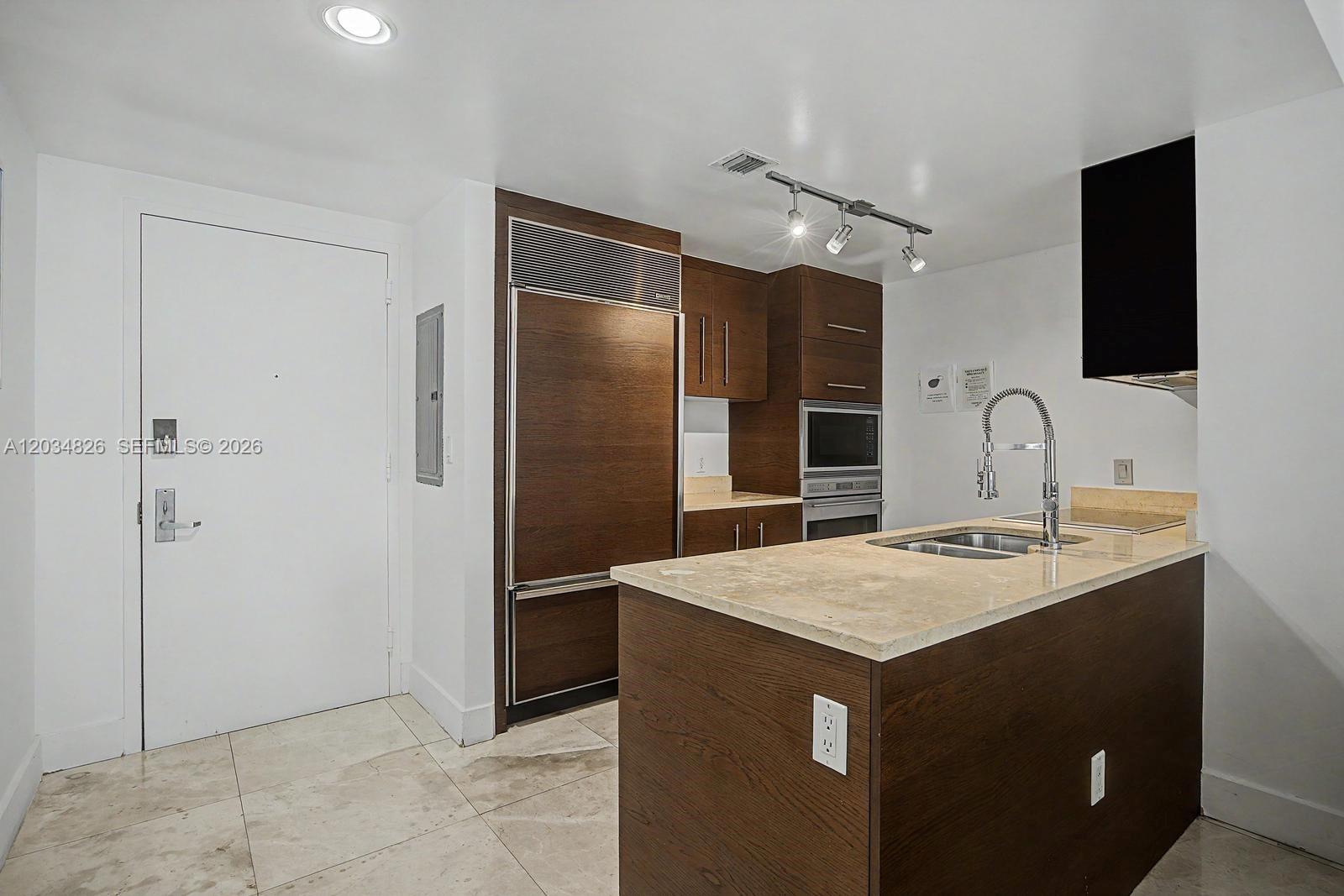 A kitchen features dark wood cabinetry, a stone countertop island, and stainless steel appliances — 485 Brickell Ave # 2209, Miami FL 33131, MIAMI, FL