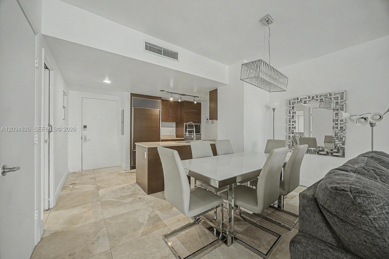 A dining area with a white table and chairs sits next to an open kitchen — 485 Brickell Ave # 2209, Miami FL 33131, MIAMI, FL