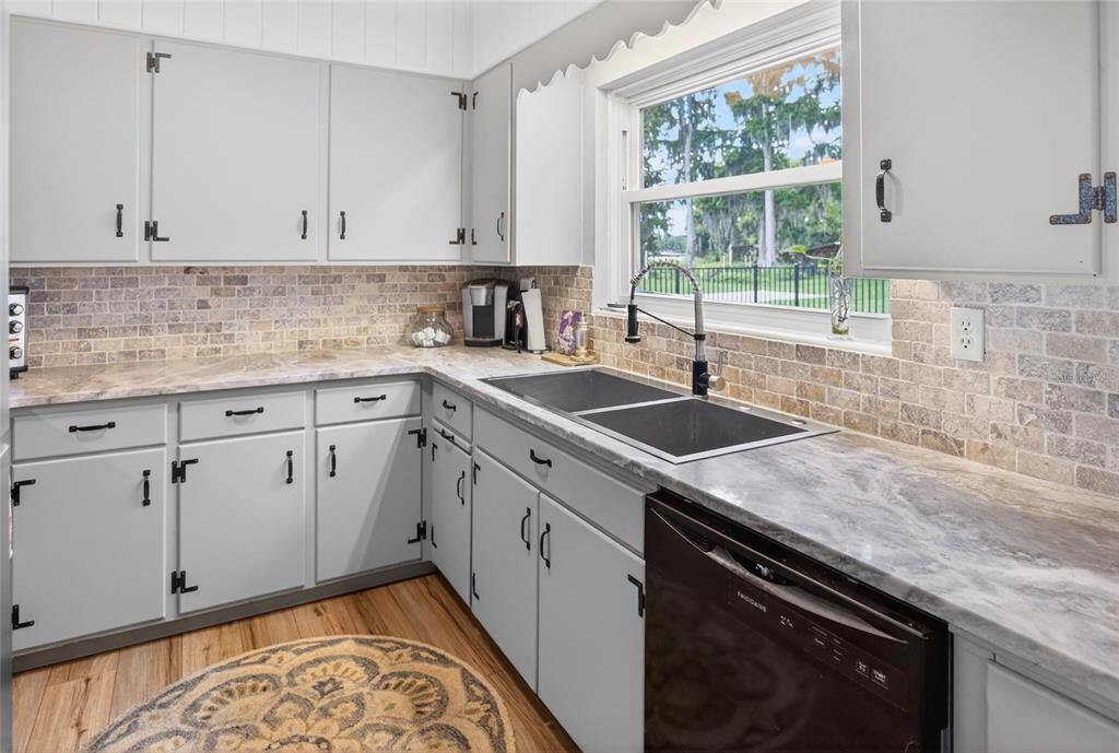 A kitchen features light gray cabinets, stone tile backsplash, marble-look countertops, and a dark dishwasher — 7588 S CRESCENT LOOP, FLORAL CITY, FL