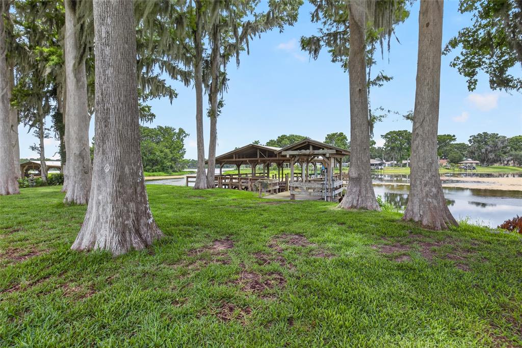 A wooden boat dock sits on a grassy lawn shaded by large trees near water — 7588 S CRESCENT LOOP, FLORAL CITY, FL