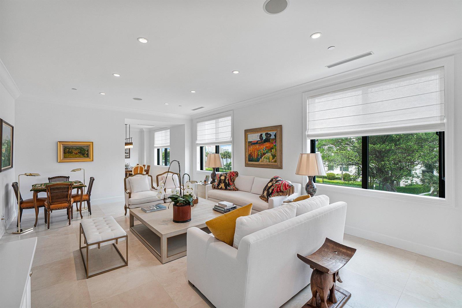 A bright living room features white sofas, a coffee table, and large windows with greenery — 150 Bradley Place # 203, Palm Beach FL 33480, PALM BEACH, FL