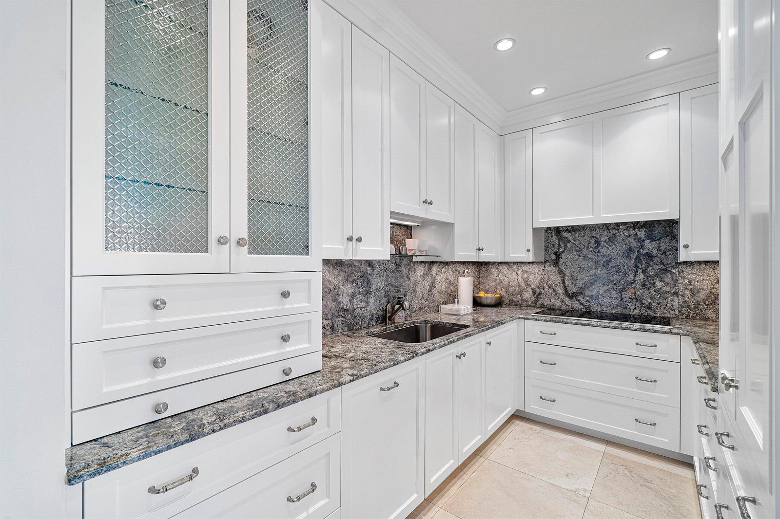 A white kitchen features granite countertops, a tiled backsplash, and glass-front upper cabinets — 150 Bradley Place # 203, Palm Beach FL 33480, PALM BEACH, FL