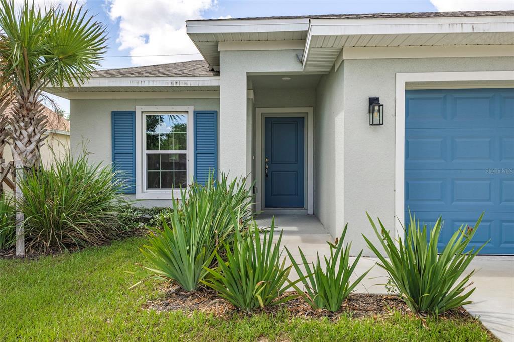 The exterior of a light-colored house features a blue front door, shutters, and garage door — 528 ROSE APPLE CIRCLE, PORT CHARLOTTE, FL