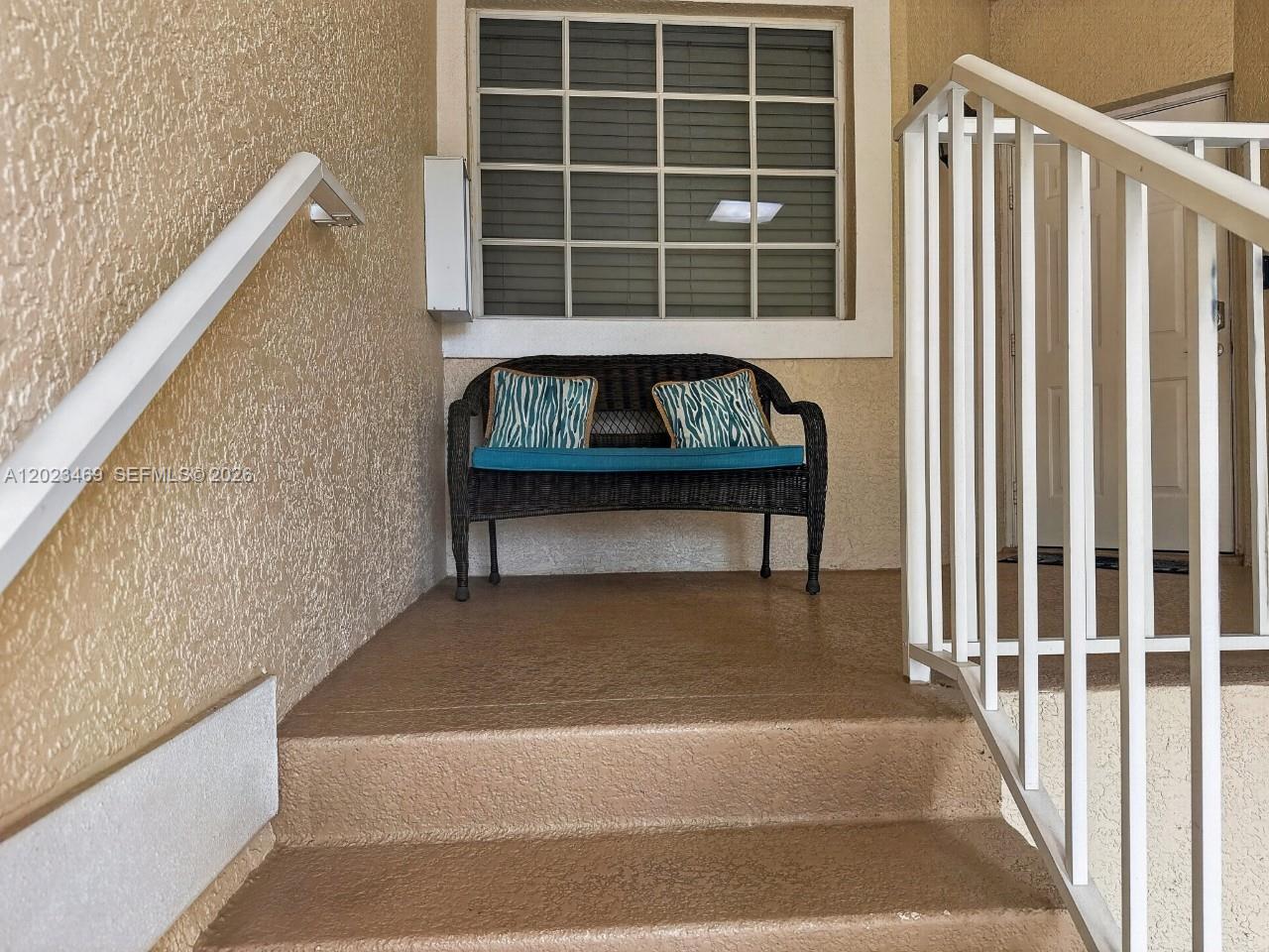 A small wicker bench with blue cushions sits on a concrete porch by stairs — NAPLES, FL