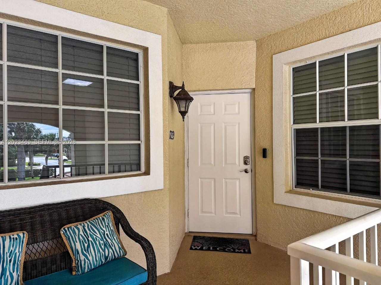 A covered entryway features a white door, two windows, and a wicker bench with cushions — NAPLES, FL