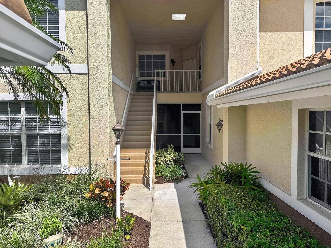An exterior view shows a beige building with a staircase leading to an upper balcony — NAPLES, FL