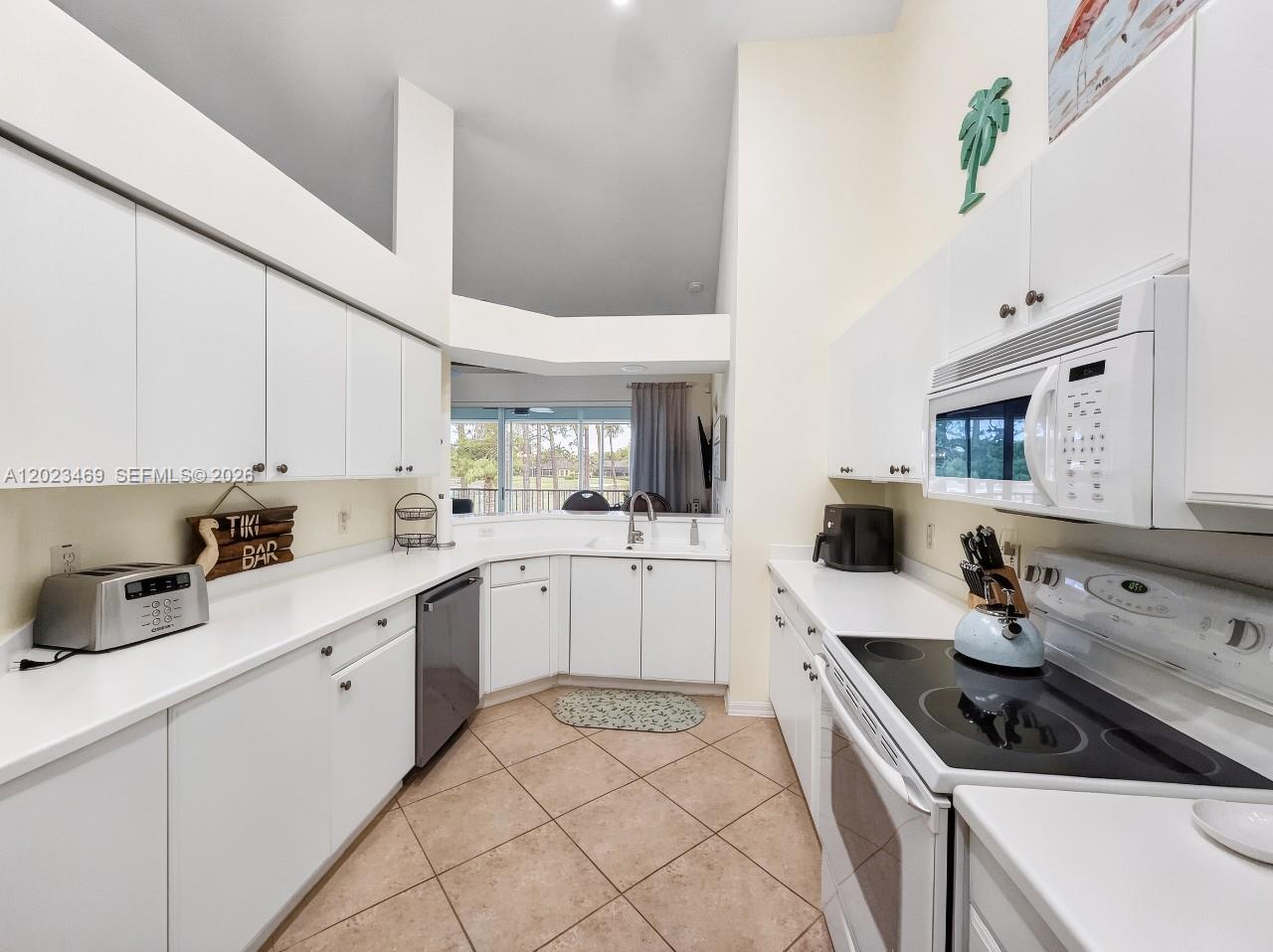A kitchen features white cabinetry, white countertops, stainless steel appliances, and beige tile flooring — NAPLES, FL