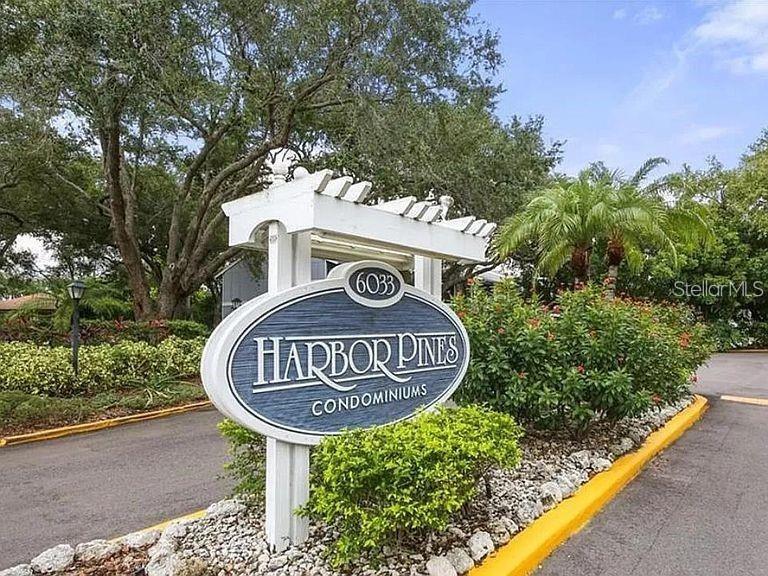 A sign for Harbor Pines Condominiums stands at the entrance of a landscaped residential property — 6033 34TH STREET W UNIT 114, BRADENTON, FL