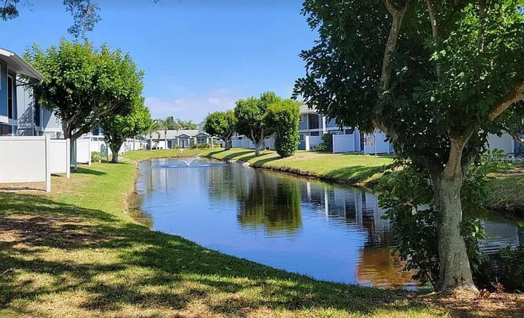 A pond with a fountain sits between residential buildings and green lawns — 6033 34TH STREET W UNIT 114, BRADENTON, FL