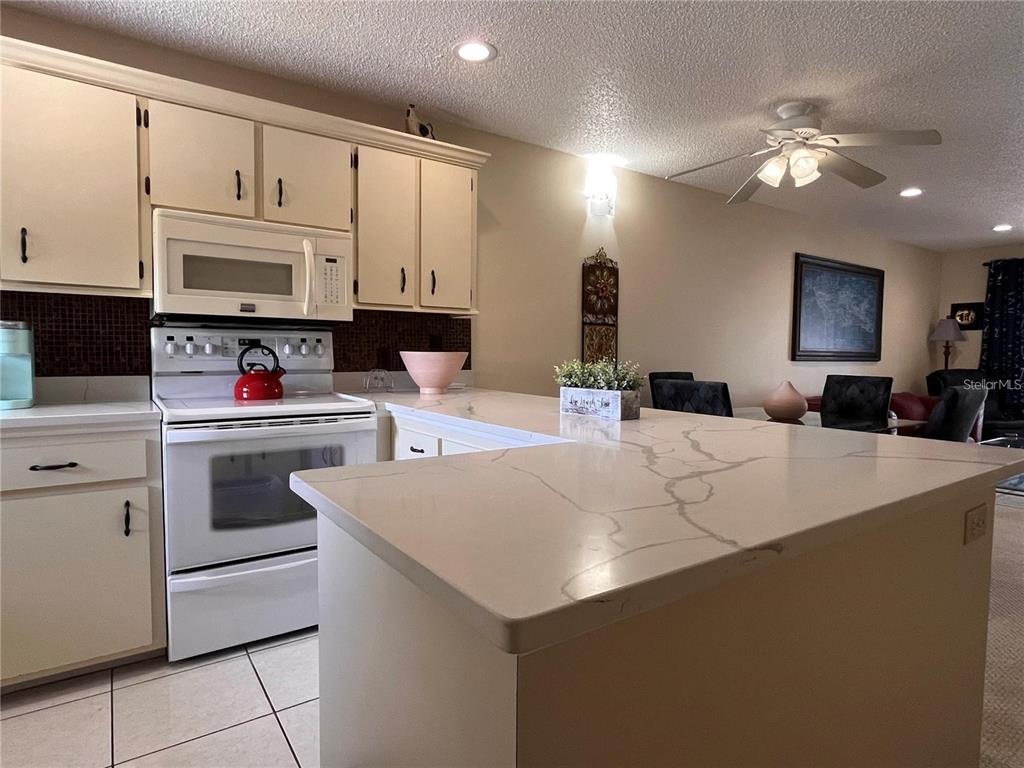 A kitchen features white cabinets, a white stove, and a light-colored quartz countertop island — 6033 34TH STREET W UNIT 114, BRADENTON, FL