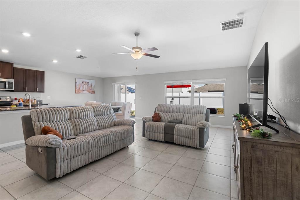 A living room with tile flooring, two gray sofas, and an open kitchen area — 889 CALICO SCALLOP STREET, RUSKIN, FL