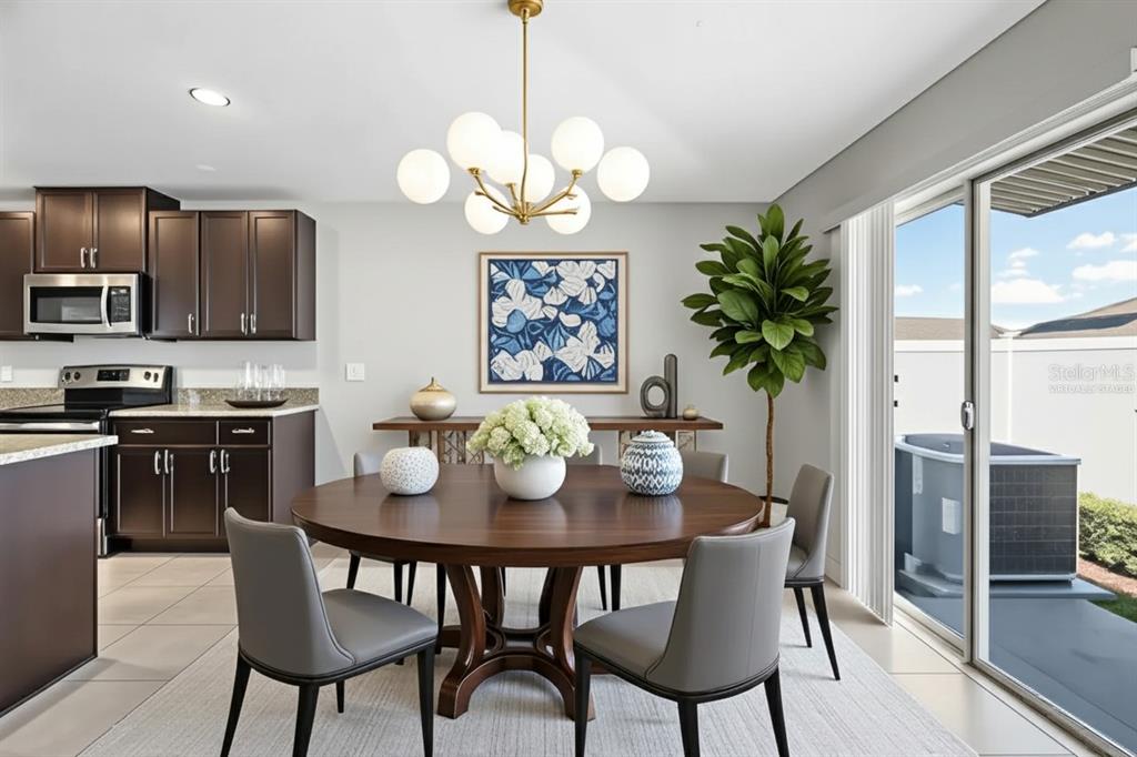 A dining area features a round wooden table, grey chairs, and a modern globe chandelier — 889 CALICO SCALLOP STREET, RUSKIN, FL